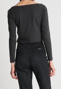 Maglietta nera a maniche lunghe con scollatura ampia, abbinata a jeans neri in denim a vita alta con dettagli unici sulle tasche posteriori.