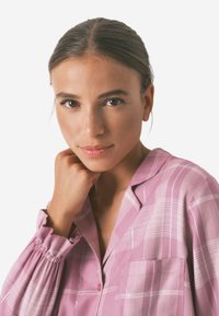 Lyserød plaid bluse med lange ærmer, flæser ved håndleddene og en lomme. Blød tekstur, knappelukning og subtil glans.