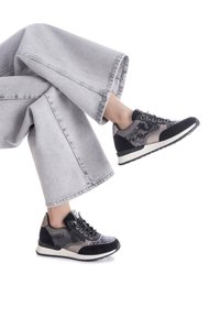 Zapatillas negras y grises con lados texturizados, acentos grises y suelas blancas. Combinadas con pantalones de mezclilla anchos en un gris pálido.