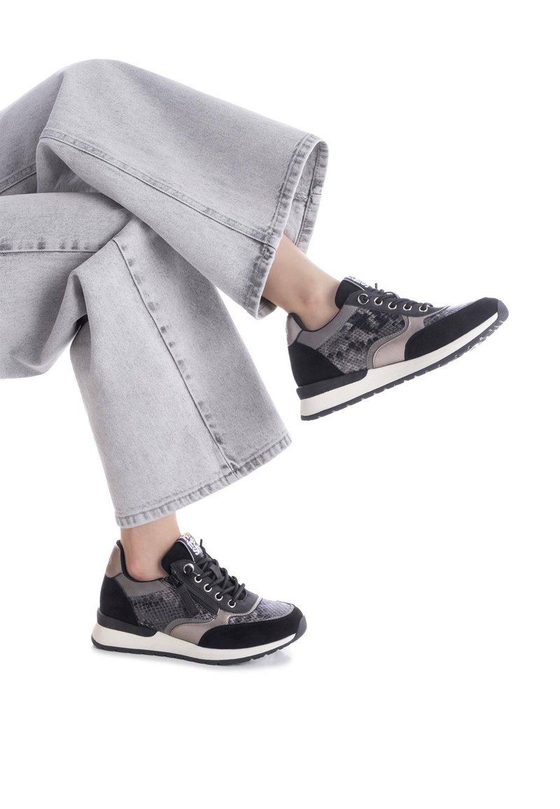 Zapatillas negras y grises con lados texturizados, acentos grises y suelas blancas. Combinadas con pantalones de mezclilla anchos en un gris pálido.