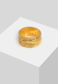 Anello d'oro con un motivo a foglia testurizzato, due bande che si intrecciano e un nome di marca inciso all'interno.