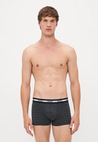 Boxer interiores negros con un patrón geométrico repetido, cinturilla elástica negra con la marca "HUGO" en blanco, diseño ajustado y tejido suave.