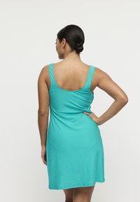 Hihaton, vartalonmyötäinen ribbineulottu mekko turkoosissa värissä, jossa pyöreä selkälinjan pääntie ja polven yli ulottuva helma. Tasainen ja sileä pinta kaikkialla.