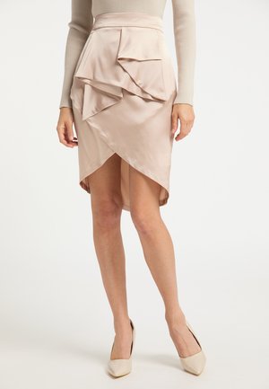 Beige satijnen wikkelrok met gelaagde ruches, gedragen met een beige top met lange mouwen en crèmekleurige puntige hakken.