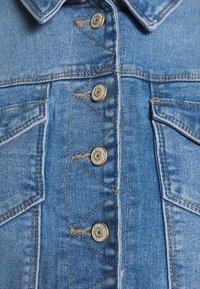 Jeansjacka i ljusblå färg. Med silverfärgade tryckknappar, spetsig krage och två framfickor med dekorativ sömnad.