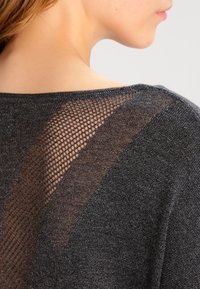 Top in maglia grigio scuro con un pannello in rete testurizzata sulla schiena, scollatura ampia e tessuto leggero e morbido.