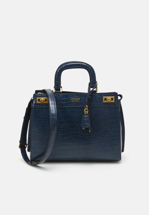 Donkerblauwe handtas met krokodillenstructuur, goudkleurige details, bovenhandvatten, schouderriem en GUESS-logo op de voorkant tegen een effen achtergrond.