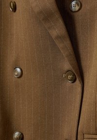 Veste de costume marron à rayures fines avec quatre boutons marron disposés en style croisé et un col à revers cranté.