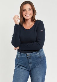 Granatowa bluzka z długim rękawem wykonana z ryshockiego materiału. Posiada okrągły dekolt oraz akcent w postaci logo na górnej części rękawa. Połączona z niebieskimi spodniami z wysokim stanem.