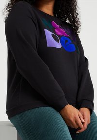 Czarna bluza z kolorowym abstrakcyjnym wzorem w odcieniach fioletu, zieleni i niebieskiego z przodu; miękka tkanina, luźny krój.