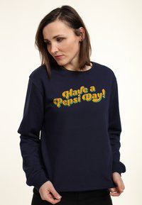 Felpa blu navy con scollatura a girocollo, caratterizzata da un design testuale colorato che recita "Buona giornata con Pepsi!" in giallo e turchese.
