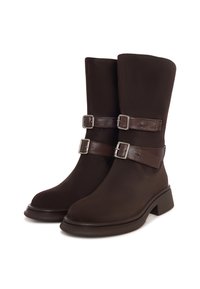 Botas marrones con una textura suave, que presentan dos hebillas ajustables y un tacón grueso. El diseño tiene un eje alto y elegante.