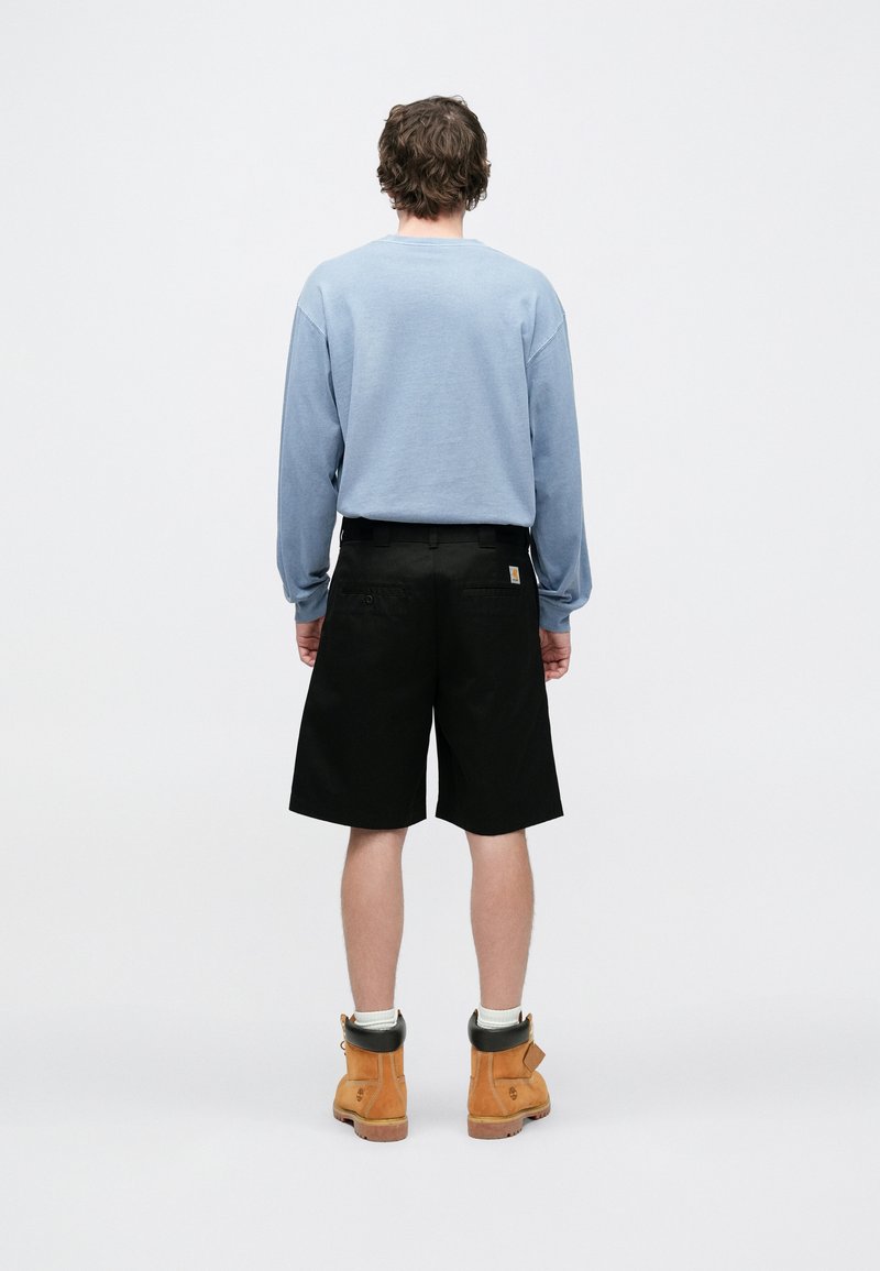 Felpa azzurro chiaro con maniche lunghe, pantaloncini neri e stivali arancioni. Il tessuto sembra morbido; i pantaloncini hanno tasche e una fascia in vita aderente.