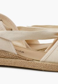 Sandali espadrillas beige con tomaia in tela, cinturini incrociati, suola a cuneo avvolta in juta e plantare liscio e piatto.