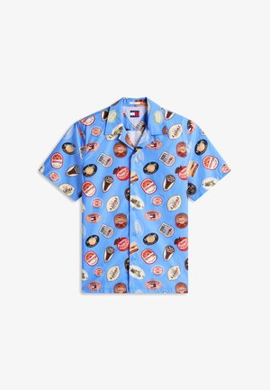 Camisa de manga corta con botones en azul claro, con estampados de logotipos circulares de estilo vintage multicolor y etiquetas dispersas por toda la prenda.