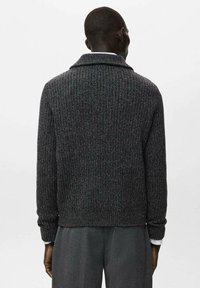 Sweter w ciemnoszarym kolorze o fakturowanym, prążkowanym wzorze, z szerokim kołnierzem i dopasowanymi mankietami, noszony na szarych spodniach, widziany od tyłu.