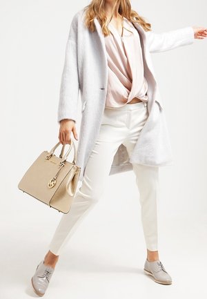 Manteau en fausse fourrure gris clair, blouse rose pâle, pantalon blanc, sac à main doré avec une étiquette, et chaussures à lacets grises, présentant une tenue superposée.