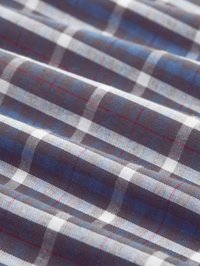 Blauw, wit, zwart en rood geruite stof met zichtbare textuur en zachte plooien die diagonale lijnen creëren.