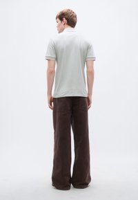 Ανοιχτό γκρι πόλο μπλουζάκι με γιακά, κοντά μανίκια και σκούρο καφέ παντελόνια με φαρδύ πόδι, που διαθέτουν πίσω τσέπες και υφή υφάσματος.