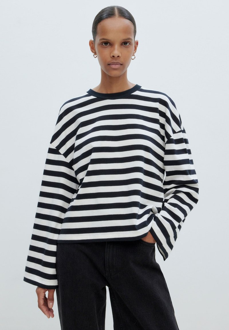 Zwart-wit gestreept shirt met lange mouwen, een ronde hals, een comfortabele pasvorm en brede mouwen. Gecombineerd met donkere spijkerbroeken.