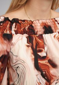 Top scollato con spalline in un tessuto leggero, caratterizzato da un motivo marmorizzato con tonalità di marrone, pesco e nero. Collo elasticizzato.