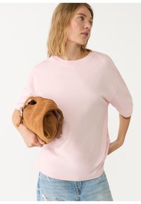 Lichtroze top met korte mouwen en een relaxte pasvorm, gecombineerd met een bruine suede clutch. De top heeft een ronde halslijn en een gladde textuur.