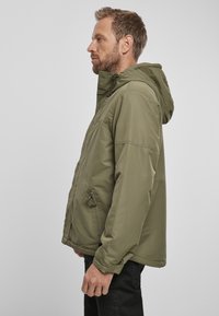 Olivno zeleni parka plašč z kapuco, dolgimi rokavi, zadrgo na sprednji strani in stranskimi žepe. Gladka tekstura z minimalističnim dizajnom, ohlapen kroj.