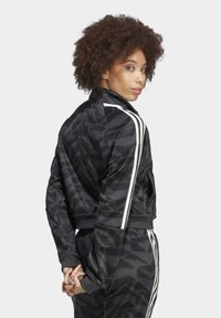 Black athletic jacket with textured pattern, featuring white stripes on sleeves. Designed with a stand collar and fitted cuffs.