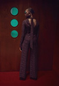 Purple lace two-piece outfit featuring a fitted long-sleeve top with a tie-back and wide-leg pants, showcasing intricate floral patterns.