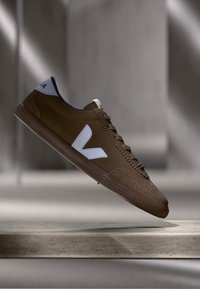 Baskets en suède marron avec logo blanc, surface texturée, design à lacets et profil bas, présentant des accents bleus au col.
