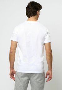 Vit kortärmad t-shirt med rund hals, avslappnad passform, mjuk textur och minimal design. Bärs med grå joggingbyxor.