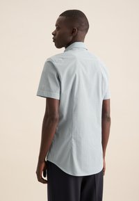 Korte mouwen geruite shirt in lichtblauw en wit. Heeft een kraag, subtiele textuur en een gebogen zoom. De achterkant toont een aansluitend ontwerp.