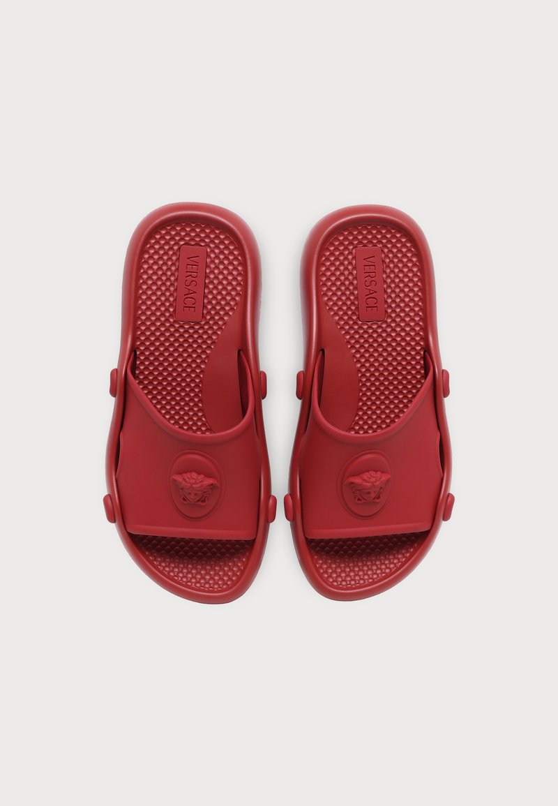 Paar rote Versace Slide-Sandalen mit strukturierten Fußbetten und Medusa-Kopf-Logos auf den Riemen, von oben auf weißem Hintergrund gezeigt.