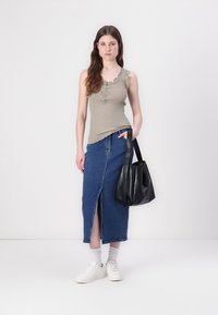 Licht olijf groen geribbelde tanktop met bloemenborduring, gecombineerd met een knielange denimrok met een split aan de voorkant, en een zwarte tote bag. Witte sneakers.