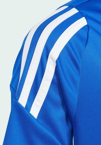 Camisa atlética azul con tres rayas blancas a lo largo del hombro, hecha de una tela suave y transpirable con un diseño ajustado.