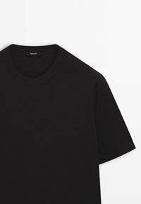 Maglietta a maniche corte nera con scollatura a girocollo e cuciture visibili su maniche e colletto, posata su uno sfondo bianco.