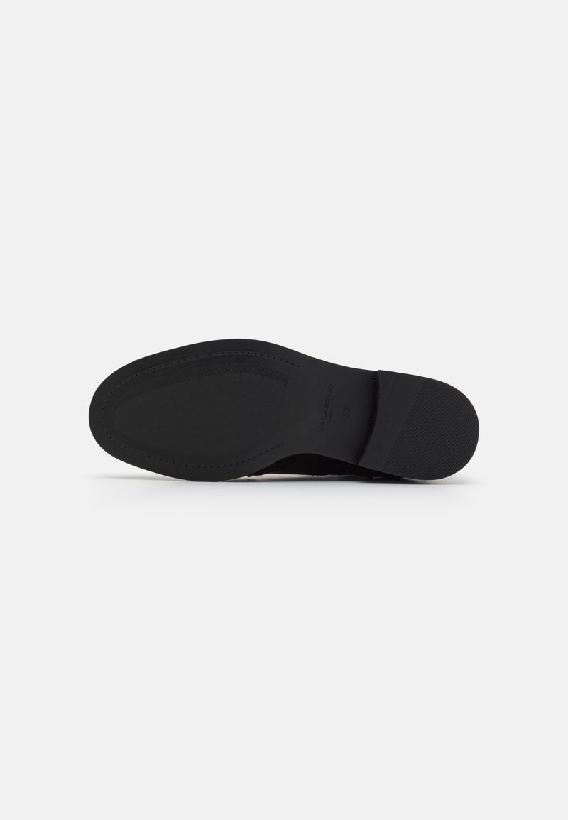 Semelle de chaussure noire avec une texture lisse, de forme rectangulaire et sans motifs visibles. Présente un léger talon et un détail de marque en relief.