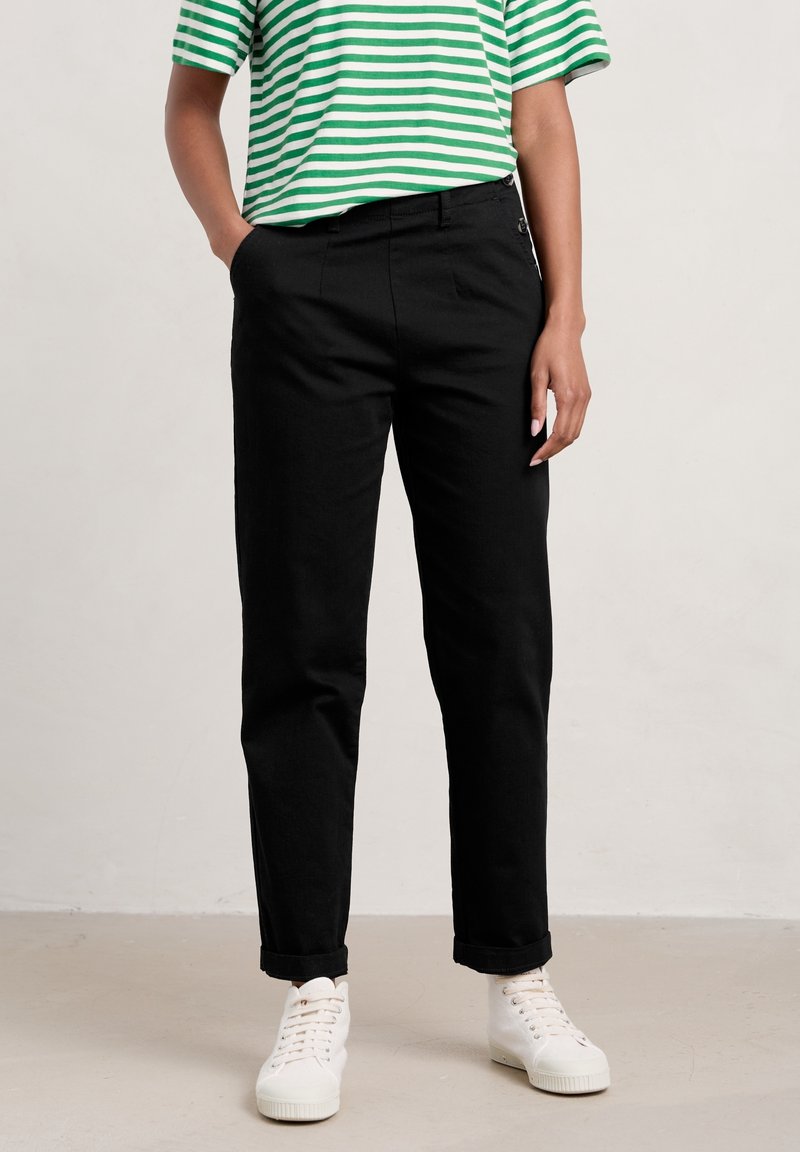 Svarta bomullsbyxor med rak passform, sidfickor och uppvikta ben, kombinerat med en grön och vit randig skjorta och vita sneakers.