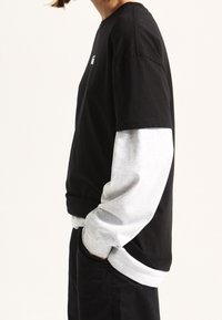 Black and gray long-sleeve shirt with a solid black body and gray sleeves. Features a crew neck and ribbed cuffs, made of soft fabric.