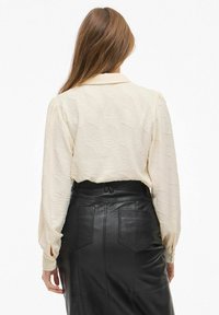 Blusa color crema con un motivo a onde e maniche lunghe, abbinata a una gonna in pelle nera con tasche posteriori e taglio dritto.
