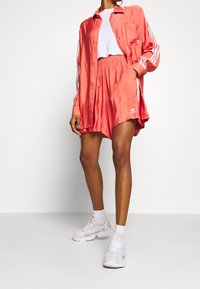 Rosenlila satin knapp-up skjorta med vita ränder på ärmarna, matchad med korta satinshorts och vita sportskor.