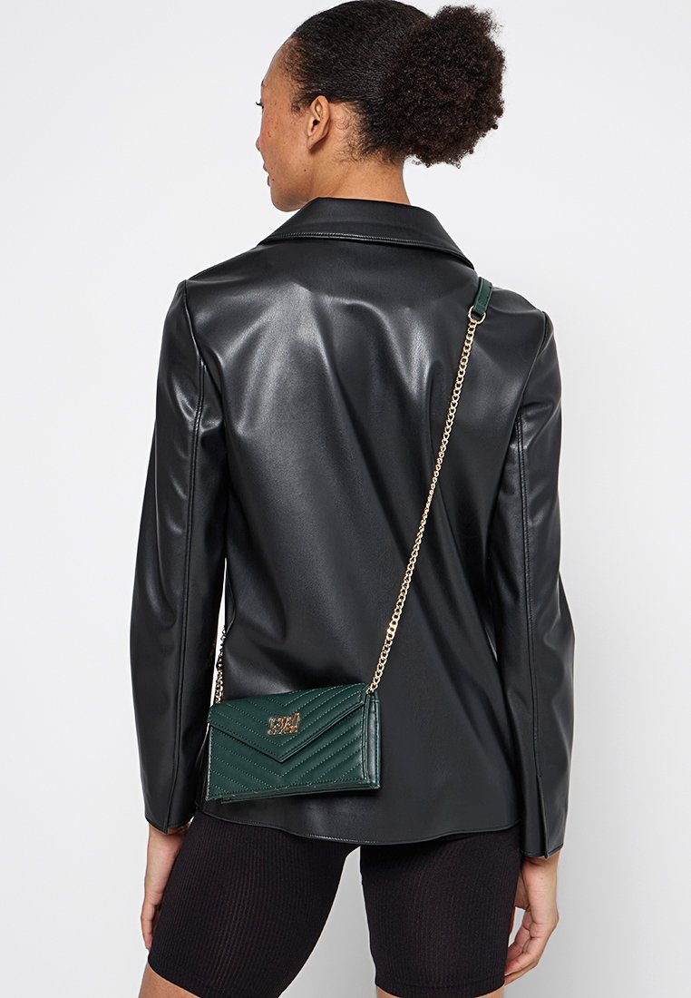 Sac de bandoulière en cuir vert foncé avec un design matelassé, une chaîne dorée et une forme rectangulaire. Fermoir décoratif sur le panneau avant.