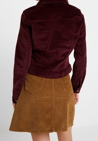 Vinrød fløjlsjakke med to brystlommer, kombineret med en tan fløjls A-formet nederdel med baglommer og lodret ribbet tekstur.