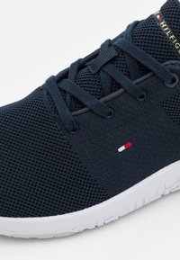 Sininen verkkokenkä valkoisella pohjalla; siinä on sävyiltään yhtenevä nauhoitus, kangaskäppyrä ja pieni punaisesta, valkoisesta ja sinisestä koostuva logo sivussa.