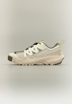 Lichtbeige en grijze Salomon trail hardloopschoen met meshpanelen, snelvetersysteem, robuuste zool en trekkoord aan de hiel.