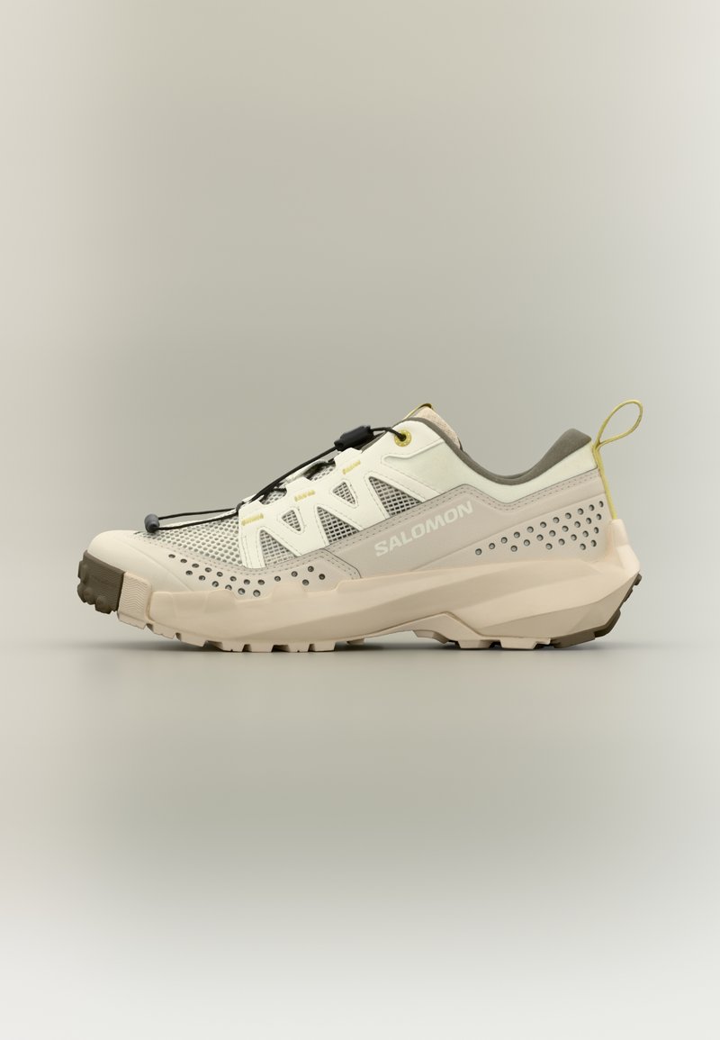Ανοιχτό μπεζ και γκρι παπούτσι ορεινού τρεξίματος Salomon με πάνελ από δίχτυ, σύστημα γρήγορου δέσιμου κορδονιών, ανθεκτική σόλα και θηλιά στο πίσω μέρος.