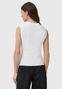 Weißes ärmelloses Oberteil aus weichem Baumwollstoff mit einem Rundhalsausschnitt; getragen mit hoch taillierten schwarzen Jeans mit Gesäßtaschen.