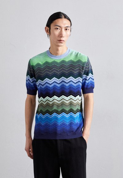 Pull en tricot à manches courtes avec un motif en chevron, présentant des couleurs verte, bleue et noire ; col rond côtelé et poignets.