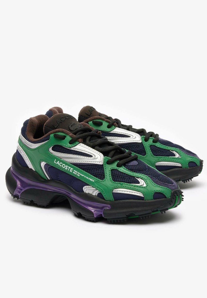 Les baskets Lacoste présentent une tige en maille verte et marine, des accents argentés, une épaisse semelle noire avec des détails violets, et des lacets noirs.