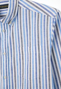 Camicia con bottoni realizzata in tessuto leggero, caratterizzata da righe verticali in blu chiaro, blu scuro e grigio. Include una tasca sul petto.